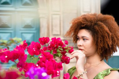 Leylak ve yeşil yapraklı kırmızı çiçeklerin arasındaki güzel kızıl saçlı kadın. Sevgi ve doğa için bakım kavramı.