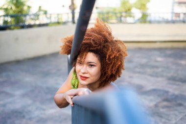 Güzel kızıl saçlı kadın bir meydanda demir korkuluğun yanında duruyor. Seyahat eden mutlu kişi.