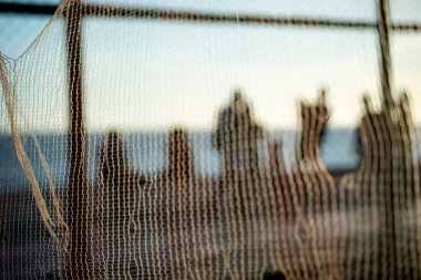 Yayaların silueti, bir ağ üzerinden, gün batımına karşı sahilin kenarında yürüyor. Fiziksel egzersiz ve zihin rahatlığı yapan insanlar..