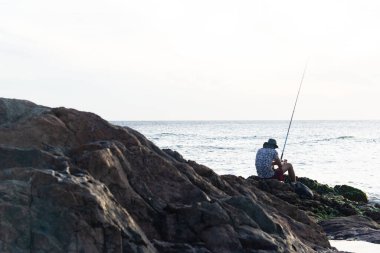 Salvador, Bahia, Brezilya - 31 Aralık 2021: Bahia 'nın Salvador kentindeki Rio Vermelho sahilinin kayalarında elinde olta olan bir balıkçının silueti.
