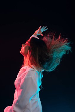 Beyaz giysiler içinde oturan ve saçlarını sağ eliyle geriye atan güzel beyaz bir kadın. Siyah arkaplanda izole.