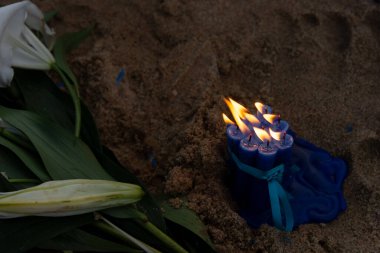 Alevli mavi mumlar ve kumsalda beyaz bir çiçek. Denizin kraliçesi Iemanja için bir hediye. Salvador, Brezilya.