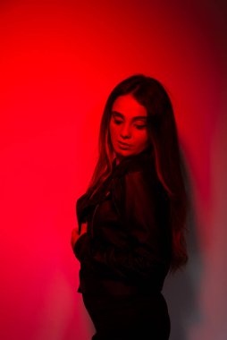 Siyah elbiseler giyen güzel genç bir manken kırmızı renkte ışıklandırılmış fotoğraf için poz veriyor. Stüdyo resmi