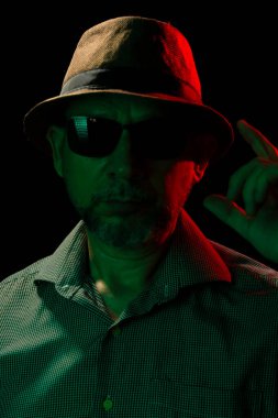 Şapka ve güneş gözlüğü takan bir adamın mistik ve sanatsal silueti. Karanlık stüdyoda portre.