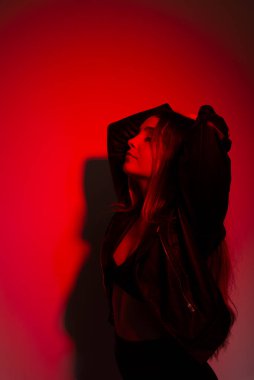 Siyah elbiseler giyen, eli başının üzerinde kırmızı resme poz veren güzel genç bir manken. Stüdyo resmi