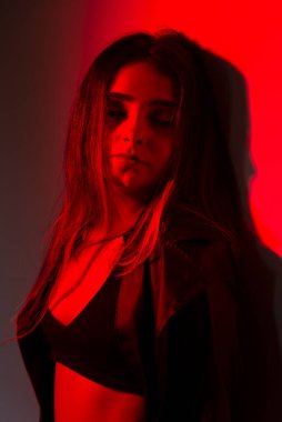 Siyah elbiseler giyen güzel genç bir manken kırmızı renkte ışıklandırılmış fotoğraf için poz veriyor. Stüdyo resmi