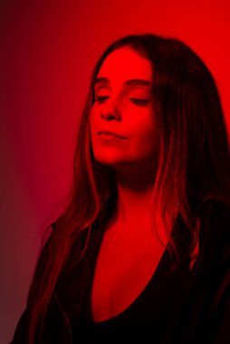 Siyah elbiseler giyen güzel genç bir manken kırmızı renkte ışıklandırılmış fotoğraf için poz veriyor. Stüdyo resmi