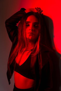 Siyah elbiseler giyen güzel genç bir manken kırmızı renkte ışıklandırılmış fotoğraf için poz veriyor. Stüdyo resmi