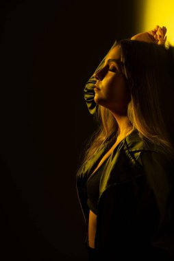 Sarı ışıklı bir duvara yaslanmış genç bir model kadın. Stüdyo fotoğrafı