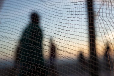 İnsan silueti, bir güvenlik ağı üzerinden, öğleden sonra bir plajın kenarında yürüyor. Soyut fotoğrafçılık kavramı.