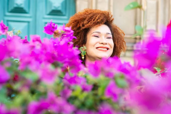 Portrait of a smiling red-haired woman among lilac and red flowers with green leaves. Confident and calm person.