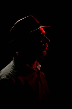 Siyah arka planda şapkalı, yüzünde kırmızı ışık olan güneş gözlüğü takan bir adam. Stüdyo resmi