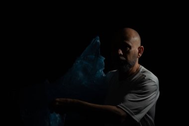 Siyah arka planda mavi plastik bir çanta tutan adam..