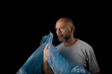 Siyah arka planda mavi plastik bir çanta tutan adam..