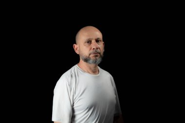 Siyah arka planda günlük kıyafetler giyen kel, sakallı bir adam..