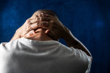 Dostum, arkası dönük, çaresiz, elleri başının üstünde, mavi bir arka planda..