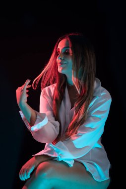 Güzel, genç, çekici, beyaz elbiseli, kırmızı bir taburede oturan beyaz bir kadın. Siyah arkaplanda izole.