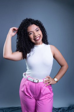 Kıvırcık saçlı, gülümseyen ve kameraya bakan güzel bir genç kadın. Gri arkaplanda izole.