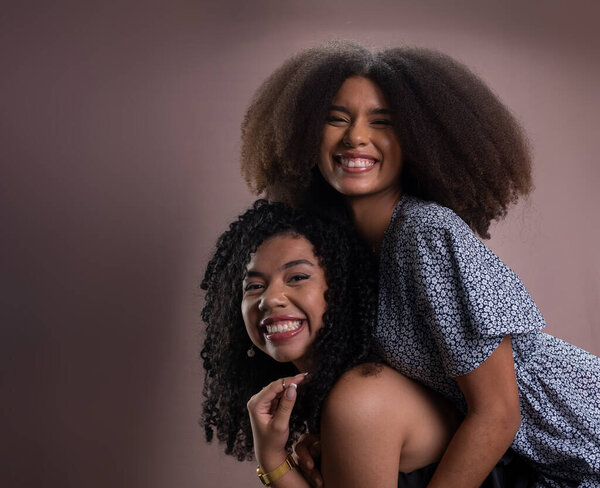 Two young, happy, beautiful friends. One carries the other on its back. Friendship and relaxation concept. Isolated on salmon-colored background.