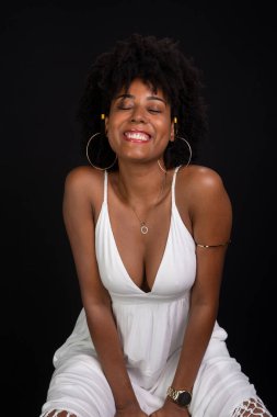 Güzel bir kadın gülümsüyor ve siyah saçlarıyla kameraya bakıyor, gülümsüyor, siyah arka planda beyaz elbiseler giyiyor..