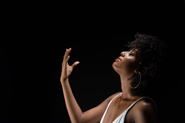 Beautiful woman, with black power hair, making movements with her arms. Wearing white clothes. Isolated on black background.