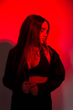 Siyah elbiseler giyen güzel genç bir manken kırmızı renkte ışıklandırılmış fotoğraf için poz veriyor. Stüdyo resmi