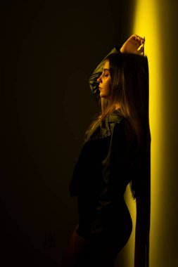Sarı ışıklı bir duvara yaslanmış genç bir model kadın. Stüdyo fotoğrafı