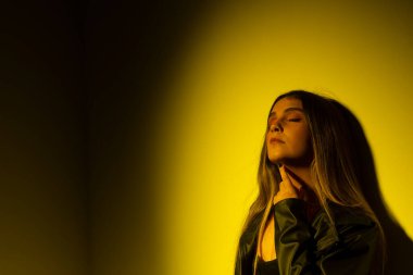 Sarı ışıklı bir duvara yaslanmış düz saçlı güzel genç bir mankenin portresi. Stüdyo fotoğrafı