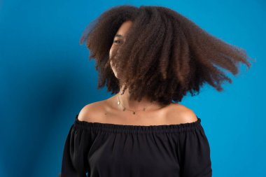 Güzel genç bir kadın siyah güç saçlarıyla hareket ediyor. Mavi arkaplanda izole.