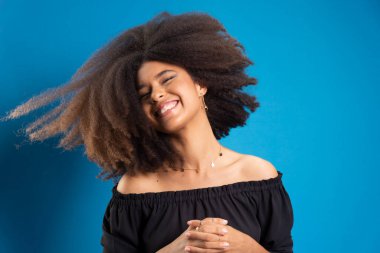 Güzel genç bir kadın siyah güç saçlarıyla hareket ediyor. Mavi arkaplanda izole.