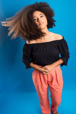 Güzel genç bir kadın siyah güç saçlarıyla hareket ediyor. Mavi arkaplanda izole.