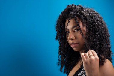 Kıvırcık saçlarına dokunan güzel bir kadının portresi. Mavi arkaplanda izole.