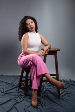 Güzel bir genç kadın, kıvırcık saçlı, stüdyoda gri bir arka planda poz veriyor..