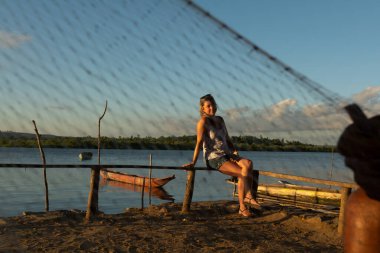 Güzel, sarışın bir kadın gün batımında tahta bir bankta oturuyor, kanolarla dolu bir nehre karşı..
