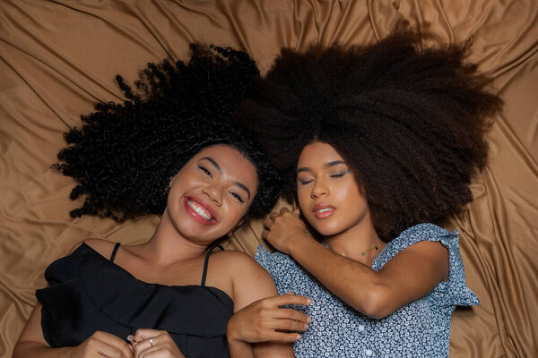 Half-closed portrait of two women lying down with their curly hair and power spread on the floor cloth. Solid friendship concept.