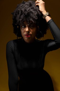 Yarı kapalı, siyah saçlı, mavi arka planda düşük ışıklı siyah elbiseler giyen, şehvetli genç bir kadının portresi..