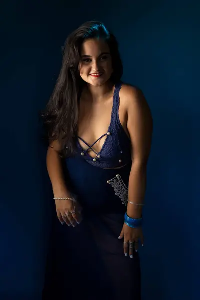 Portrait of beautiful woman with black hair, cheerful, confident, in a blue dress, looking at the camera. Isolated on dark blue background.