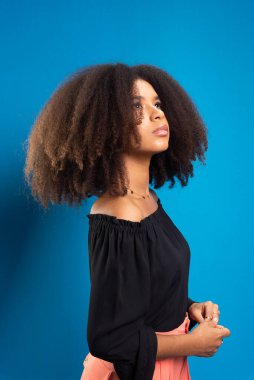 Siyah saçlı, sıradan kıyafetler giyen güzel bir genç kadın. Mavi arkaplanda izole.