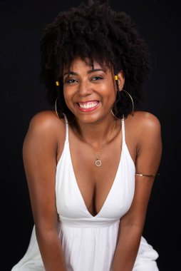 Güzel bir kadın gülümsüyor ve siyah saçlarıyla kameraya bakıyor, gülümsüyor, siyah arka planda beyaz elbiseler giyiyor..