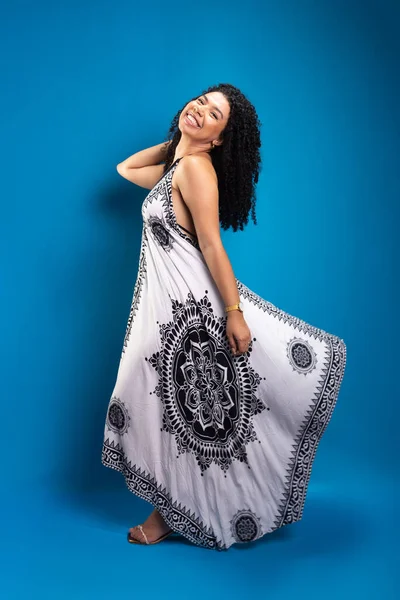 stock image Beautiful young woman, with curly hair, standing, posing for a photo in a long dress. Isolated on blue background.