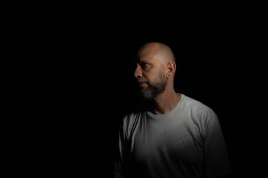 Siyah arka planda sakallı ve kel bir adamın portresi.