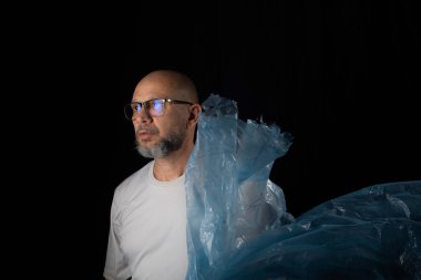 Siyah arka planda mavi plastik bir çanta tutan adam..