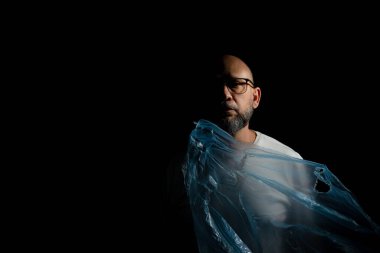 Siyah arka planda mavi plastik çantalı kel, sakallı bir adam..