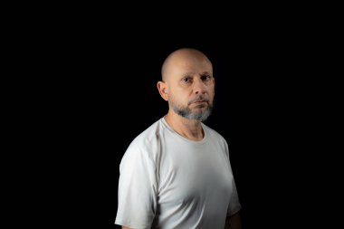 Siyah arka planda günlük kıyafetler giyen kel, sakallı bir adam..