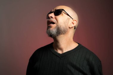 Güneş gözlüklü, kel, kendine güvenen beyaz bir adam. Kırmızı arkaplanda izole.