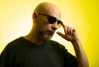 Beyaz, kel, güneş gözlüğü takıyor, ciddi ve düşünceli. Sarı arkaplanda izole edilmiş.