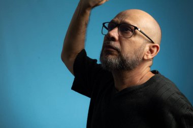 Yakışıklı, kel, sakallı, gözlüklü adam yukarı bakıyor. Mavi arkaplanda izole.