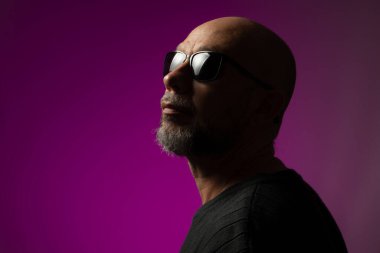 Güneş gözlüklü, kel ve sakallı yakışıklı adam kameraya doğru bakıyor. Pembe arka planda izole edilmiş.