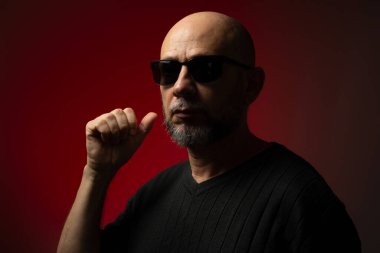 Güneş gözlüklü, yakışıklı, kel ve sakallı bir adam. Ciddi ve kendine güvenen bir poz veriyor. Kırmızı arkaplanda izole.