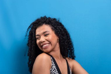 Kıvırcık saçlı, gülümseyen güzel bir kadın. Mavi arkaplanda izole.
